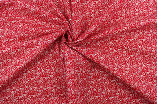 This fabric features a whimsical vine and floral design in white set against a red background.