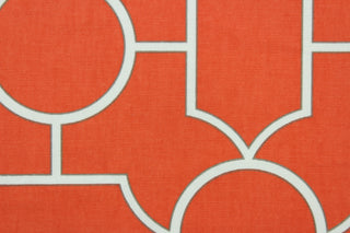  This fabric features a geometric design in white outlined in gray set against a bright orange background. 