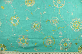 Suzani features an embroidered ethnic design in shades of green and gold against an aqua background.  Uses include drapery, pillows, light upholstery, table runners, bedding, headboards, and home décor.