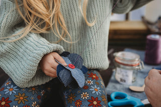 A girl sewing a red button onto some blue fabric pieces