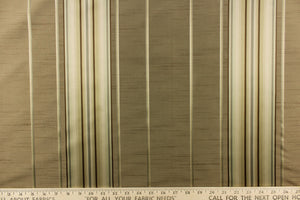 This stunning yarn dyed fabric features a multi width striped pattern in gold, brown, gray, and cream or champagne.