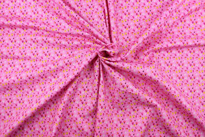 This fabric features a tiny seedlings design in yellow, white, orange, dark pink, black, and brown set against a pink background.