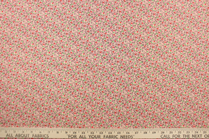 This fabric features a dainty floral design in green, white, brown and red set against a pink background. 