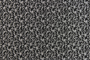 This fabric features a tiny floral vine design in white set against a black background.