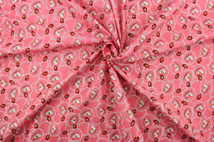 This quilting fabric features a cowboy/cowgirl theme with a rocking horse, rope and hat design in green, dark red, and white set against a medium pink background. 