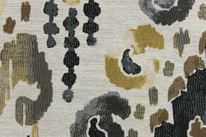 This jacquard fabric features an Aztec design in  gold, black, gray, and brown set against a off white. 