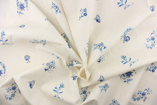 A floral blue blossom and butterfly pattern set against a creamy particulate background