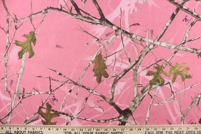 This camo fabric features realistic branches and leaves in brown, gray and black against a pink background. 