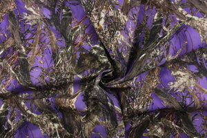 This camo fabric features realistic branches and leaves in varying shades of brown, gray, white and black against a purple background. 