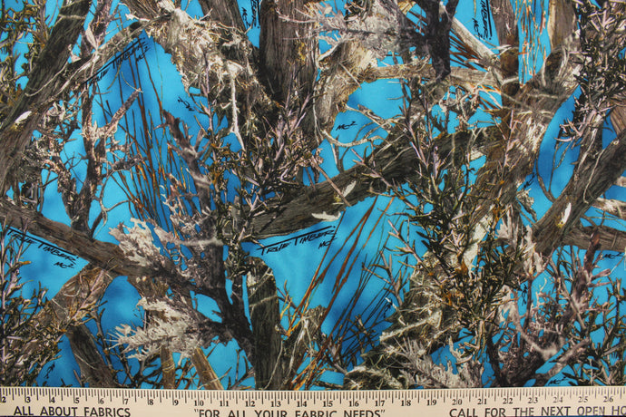 This camo fabric features realistic branches and leaves in varying shades of brown, gray, white and black against a blue  background.  