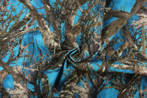 This camo fabric features realistic branches and leaves in varying shades of brown, gray, white and black against a blue  background.  