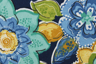 This outdoor fabric features a floral design in varying shades of blue, green, teal, pale yellow, and a dark mustard tone with hints of black and white on a navy blue background.