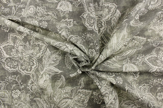 This fabric features a whimsical floral design in a off white against a gray with green undertones.