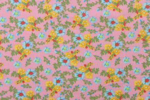 This soft quilting print features a beautiful floral design in blue, yellow, red, and green against a pink background. 
