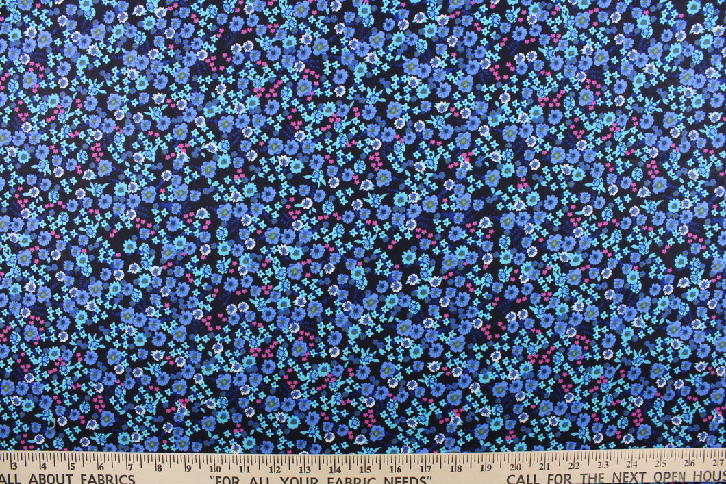 This quilting print features a beautiful floral design in shades of blue, blue green, pink, and white against a dark navy background. 