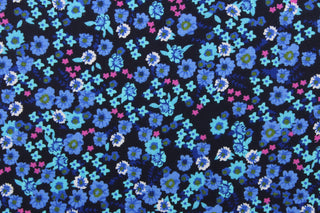 This quilting print features a beautiful floral design in shades of blue, blue green, pink, and white against a dark navy background. 