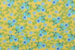This soft quilting print features a beautiful floral design in shades of blue with hints of purple and green against a yellow background.