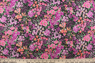 This quilting print features a floral design in varying shades of pink, purple, green and pale orange with hints of white against a black background. 