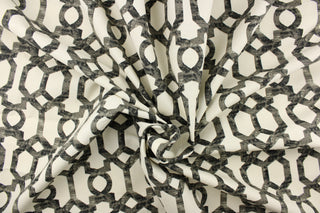  This fabric features a  geometric design in black and gray tones on an off white background. 