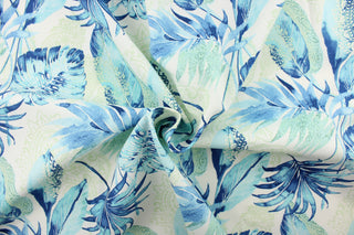  This outdoor fabric features a floral design in blue, pale green, and  turquoise against a white background. 