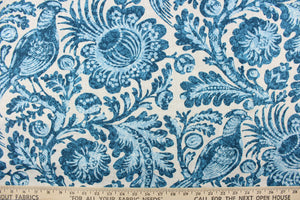 This outdoor fabric has a floral and bird design in varying shades of blue against a pale gray background. 