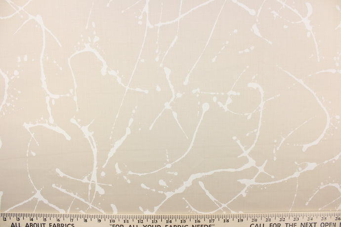 This fabric features a paint splatter design in white against a sand background. 
