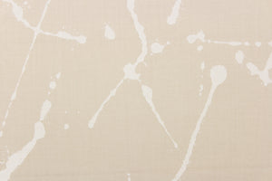 This fabric features a paint splatter design in white against a sand background. 