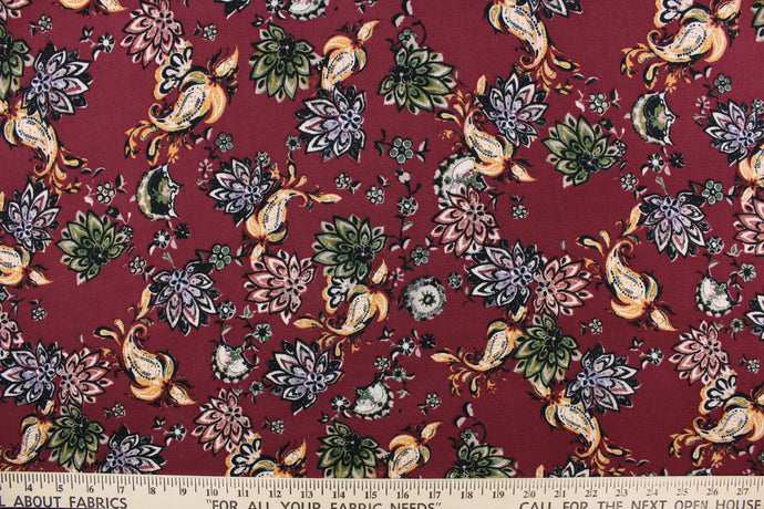 This georgette fabric features a floral design in green, golden yellow, white, black, and pale purple against a maroon background. 