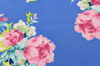 This georgette fabric features a floral design in pink, yellow, white, green, and blue against a cornflower blue.