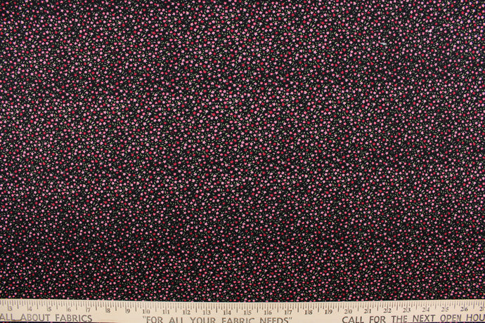 This jersey fabric features a dainty floral design in pink, green, and dark pink against black background.
