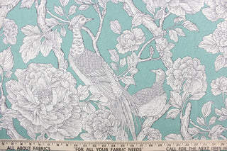 This fabric features a bird and floral design in  white and gray against an aqua background. 