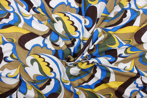 This jersey fabric features an abstract design in blue, yellow. olive green, brown, tan and white. 