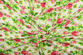This jersey fabric features a floral design in pink, red, green, and off white. 