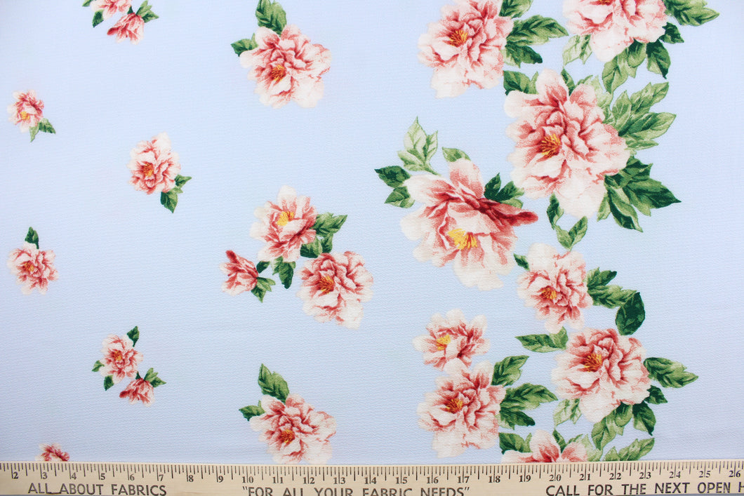  This georgette fabric features a floral design in pink, red, white, and green with hints of golden yellow against a periwinkle blue background. 
