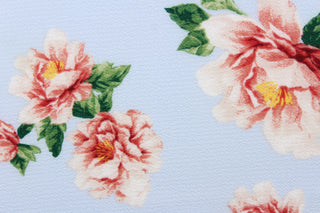  This georgette fabric features a floral design in pink, red, white, and green with hints of golden yellow against a periwinkle blue background. 