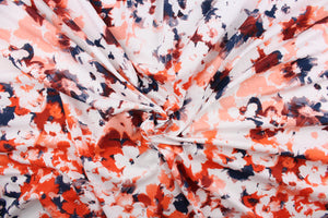This jersey fabric features an abstract design in orange, dark blue, dark red, peach, gray and white. 