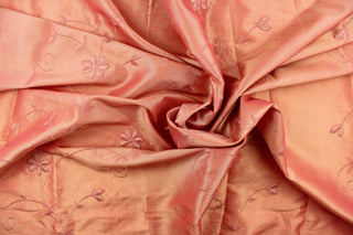  This beautiful fabric features an embroider floral design in a iridescent peachy pink with gold tones. 