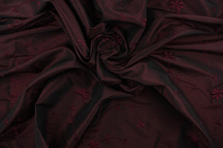 This beautiful fabric features an embroider floral design in a iridescent deep wine purple .