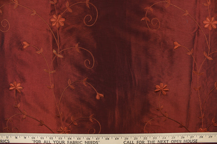 This beautiful fabric features an embroider floral design in a iridescent rustic red .