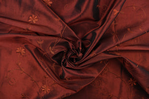 This beautiful fabric features an embroider floral design in a iridescent rustic red .