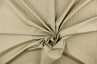 This yarn dye stripe fabric features a small plaid or checkered design in light khaki and taupe with hints of greens .
