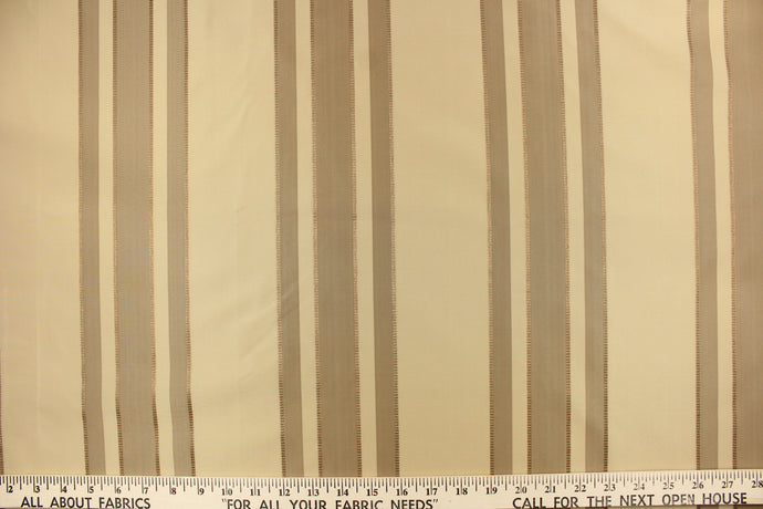  This fabric features a multi width stripe design in beige tones, tan and gold.