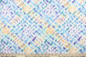 This outdoor fabric features a diagonal plaid design in purple, blue , yellow, orange, and turquoise against a white background.