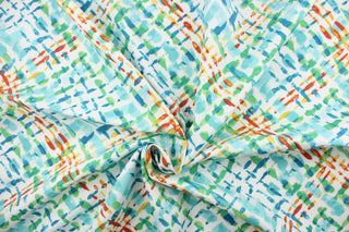 This outdoor fabric features a diagonal plaid design in blue, dark orange, yellow, and green against a white  background. 