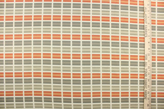 This fabric features a plaid design in orange, gray, taupe, and off white . 