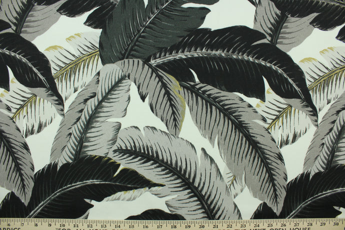 This fabric features palm tree leave design in black, gray, and golden tan set against a white background . 