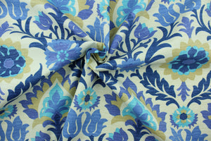  This outdoor fabric features a floral design in tan, turquoise, blue, and hints of purple set against a pale beige background.
