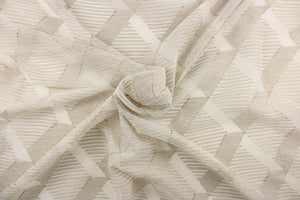 This sheer fabric features a geometric design in gold, gray, and cream against a dull white . 