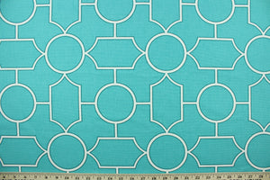  This fabric features a geometric design in white outlined in green set against a turquoise blue background.