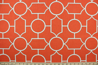  This fabric features a geometric design in white outlined in gray set against a bright orange background. 